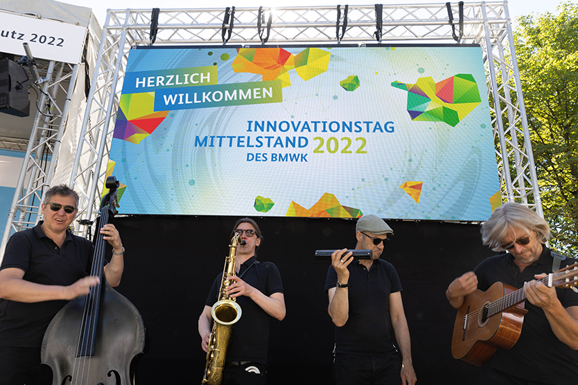 Eine Band spielt vor einer LED-Leinwand mit dem Schriftzug Innovationstag Mittelstand des BMWK 2022
